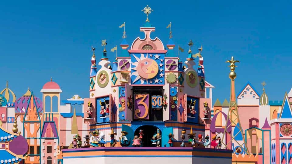 Façade colorée de l’attraction It’s a Small World à Fantasyland, grande horloge centrale entourée de silhouettes de poupées représentant les enfants du monde