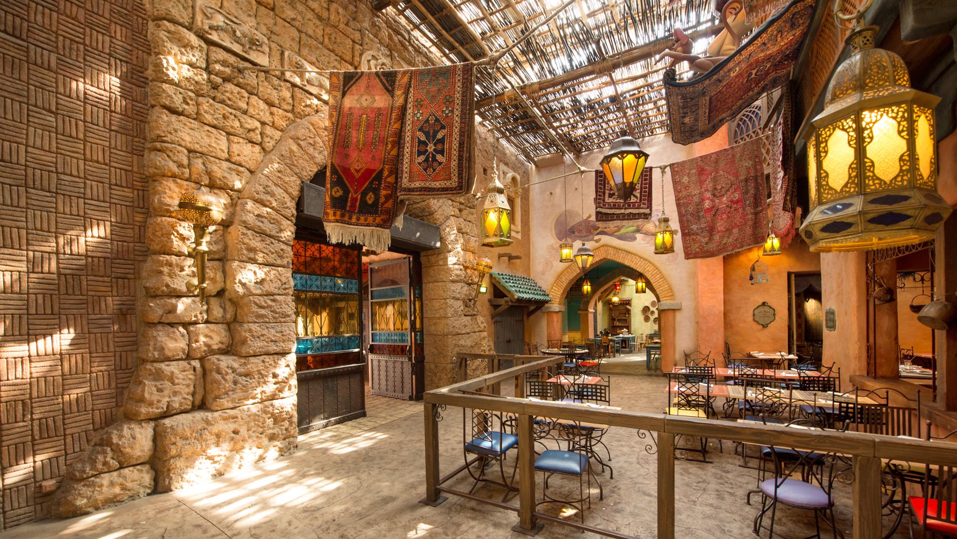 Salle du restaurant Agrabah Café dans Adventureland, décor de palais oriental avec lanternes dorées, mosaïques colorées et tapis aux motifs arabesques