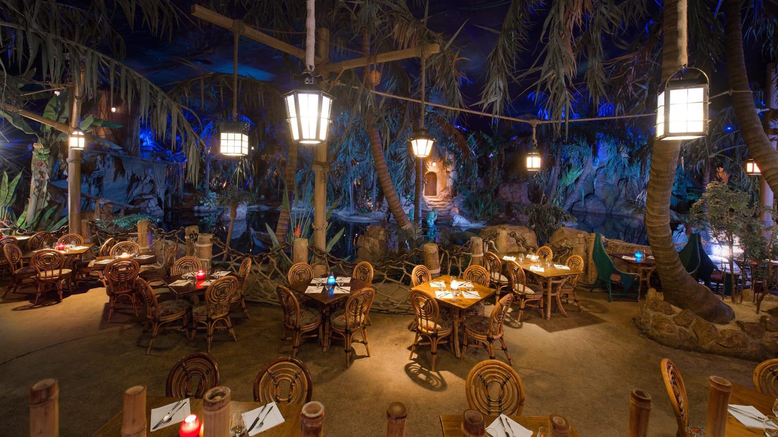 Intérieur du Captain Jack’s Restaurant des Pirates en Adventureland, lagon éclairé aux torches avec bateaux pirates de l’attraction naviguant à quelques mètres des tables