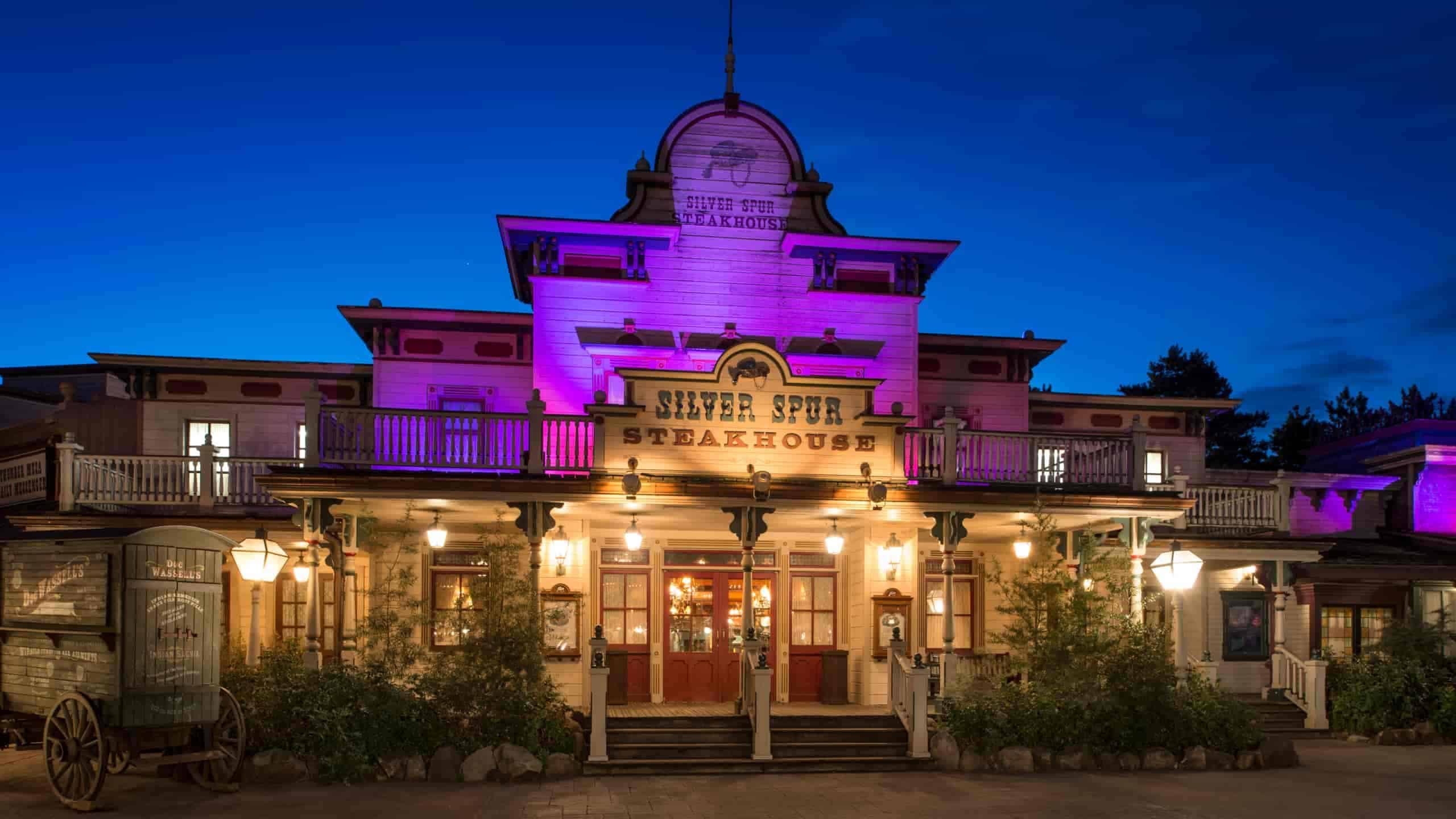 Salle principale du Silver Spur Steakhouse en Frontierland, décor de saloon Far West élégant avec boiseries sombres, tableaux de cowboys et éclairage aux chandelles