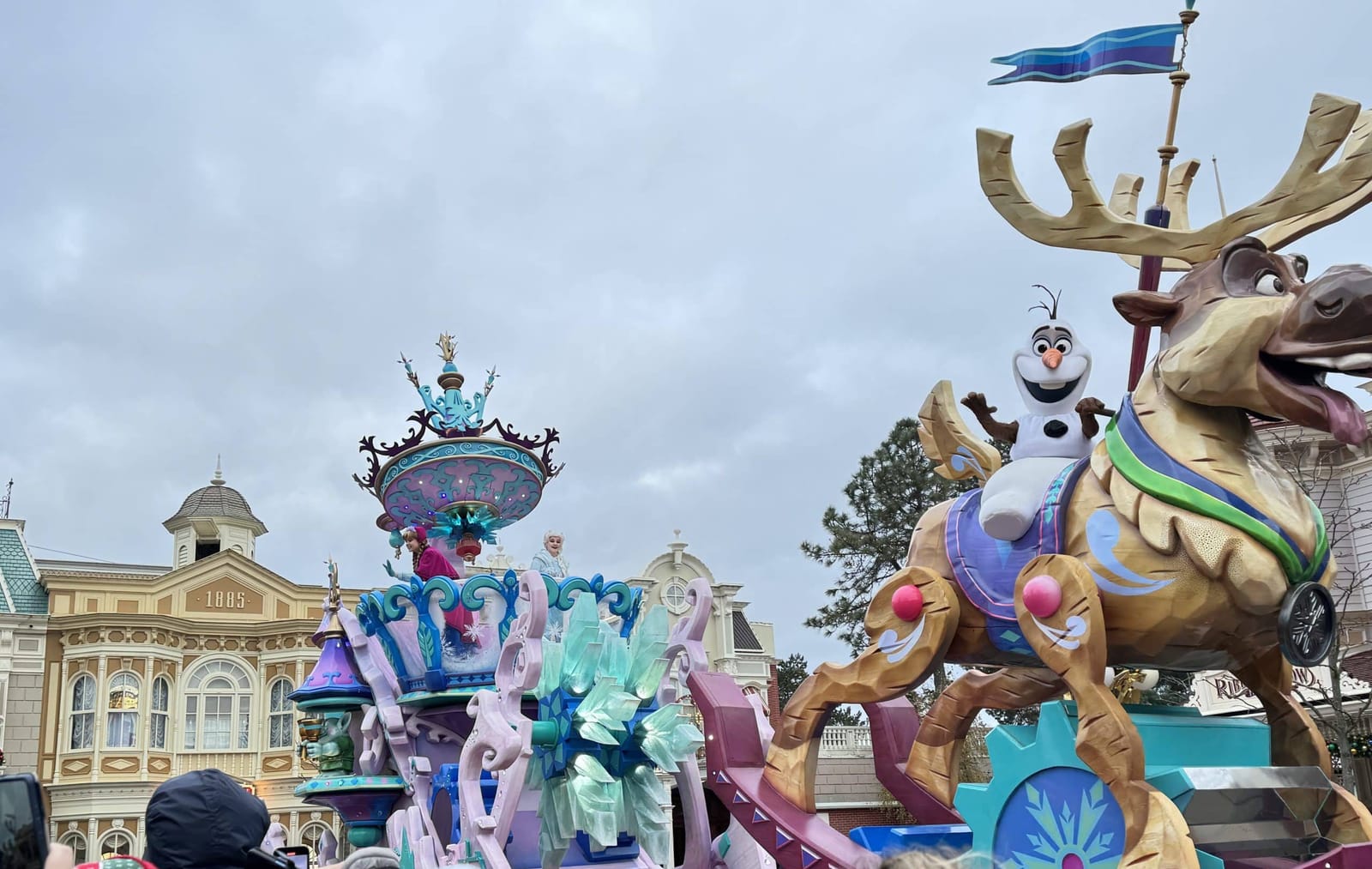 Char de la parade de la Reine des Neiges sur Main Street USA, Elsa et Anna en costume d'Arendelle entourées de danseurs sur fond de décors glacés